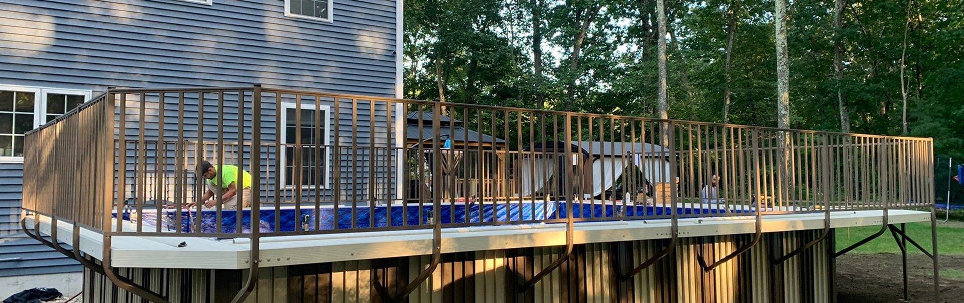 A bright suburban backyard with a swimming pool, patio seating, and a white house under clear skies.